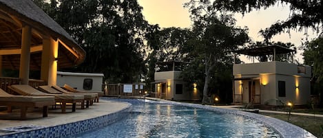 A swimming pool with lounge chairs and a thatched-roof structure.