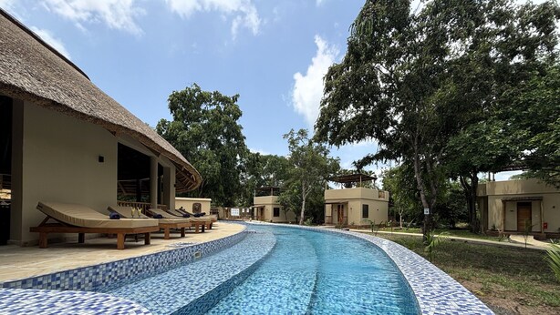 A swimming pool with blue mosaic tiles, lounge chairs, and a thatched-roof building. - Africa Safari Nyerere (Selous Game Reserve)