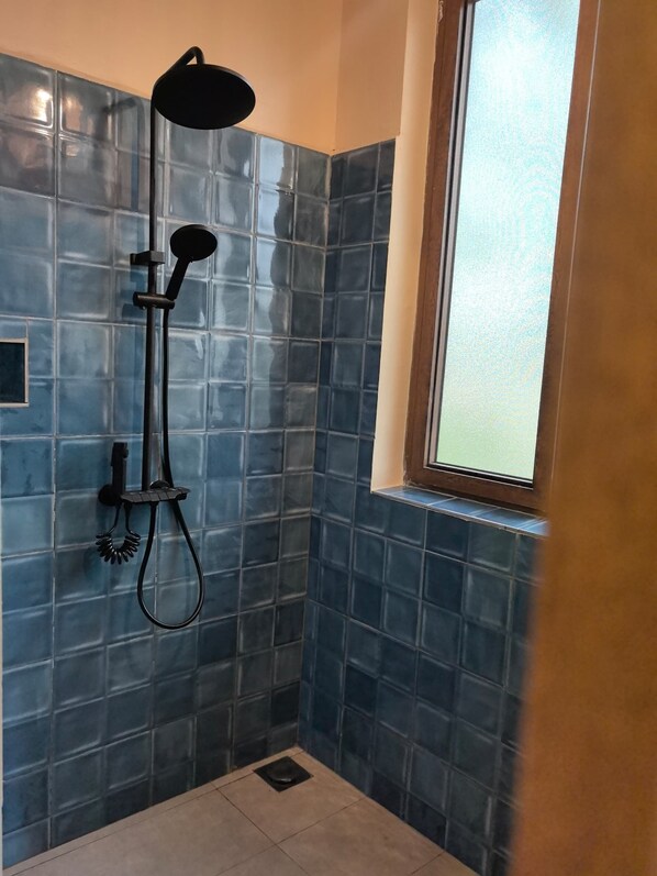 Ducha con cabezal de ducha de mano, control en la pared y una ventana arriba.
