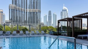 Ein Pool auf dem Dach mit Liegestühlen und Sonnenschirmen, umgeben von Hochhäusern.