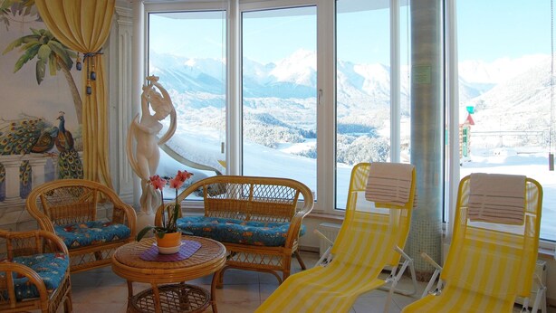 A room with large windows, wicker furniture, and a statue. - Apartment in Arzl With Wellness Area (Arzl im Piztal)