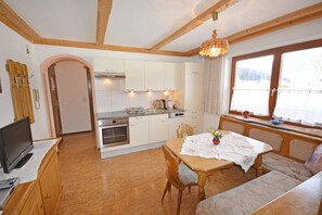 A cozy kitchen with wooden cabinets, a dining table with a lace tablecloth, and a window with a view of the outdoors.