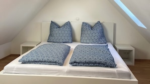 Un dormitorio moderno con techo inclinado, tragaluz y cama con almohadas estampadas.