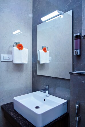 A modern bathroom with a white sink, a mirror, and two towels with orange flowers. - VILLA GRAND HOTEL NEAR BENGALURU AIRPORT (Bengaluru)