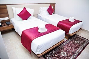 Two single beds with white bedding and red accents, a wooden headboard, a telephone on the nightstand, and a patterned rug on the floor. - VILLA GRAND HOTEL NEAR BENGALURU AIRPORT (Bengaluru)