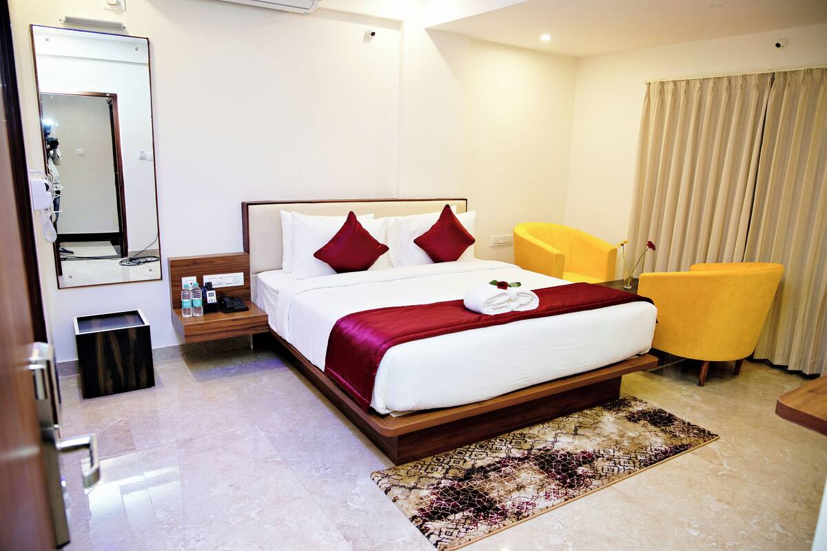 A hotel room with a large bed, a bedside table with a phone, a chair, and a mirror.