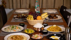 Een eettafel gedekt met verschillende gerechten, waaronder rijst, biryani en een fruitmand.