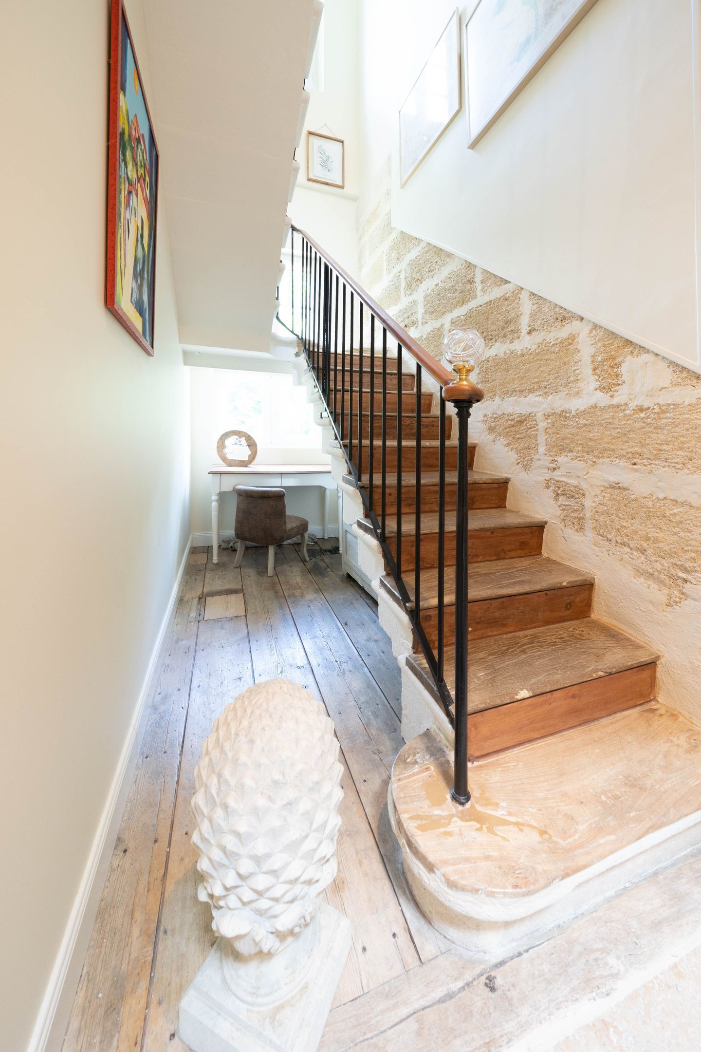 A staircase with wooden steps and a black railing, leading to a landing with a white desk and chair.