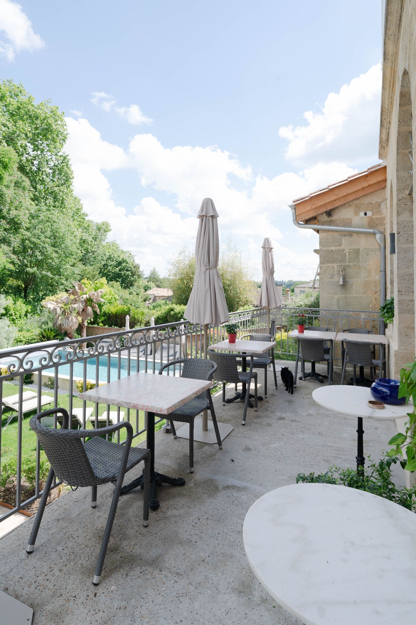 Un patio al aire libre con mesas y sillas, una piscina y vistas a la vegetación.
