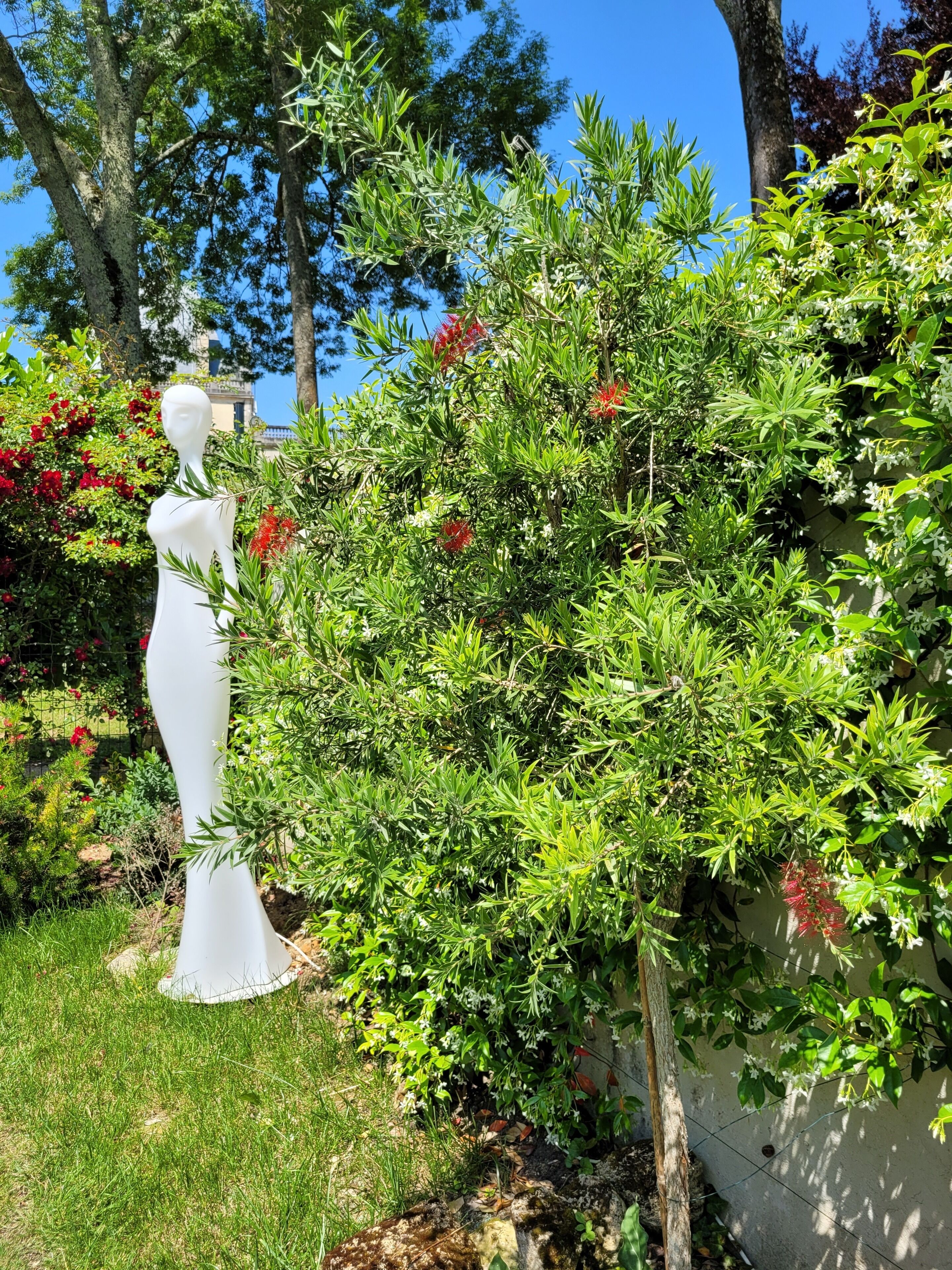 A garden with a white statue, lush greenery, and flowering plants.