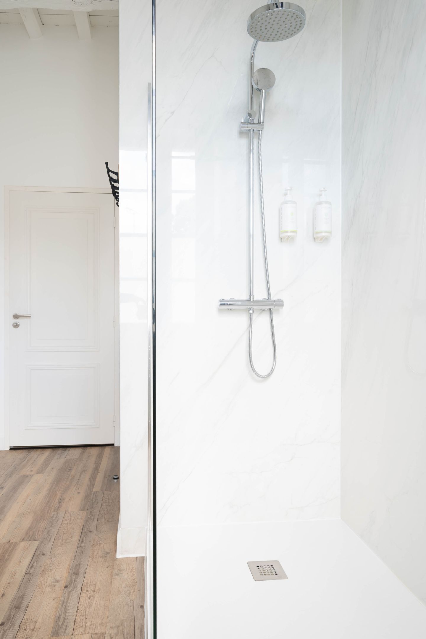 A modern bathroom with a glass shower enclosure, a white door, and a marble wall.