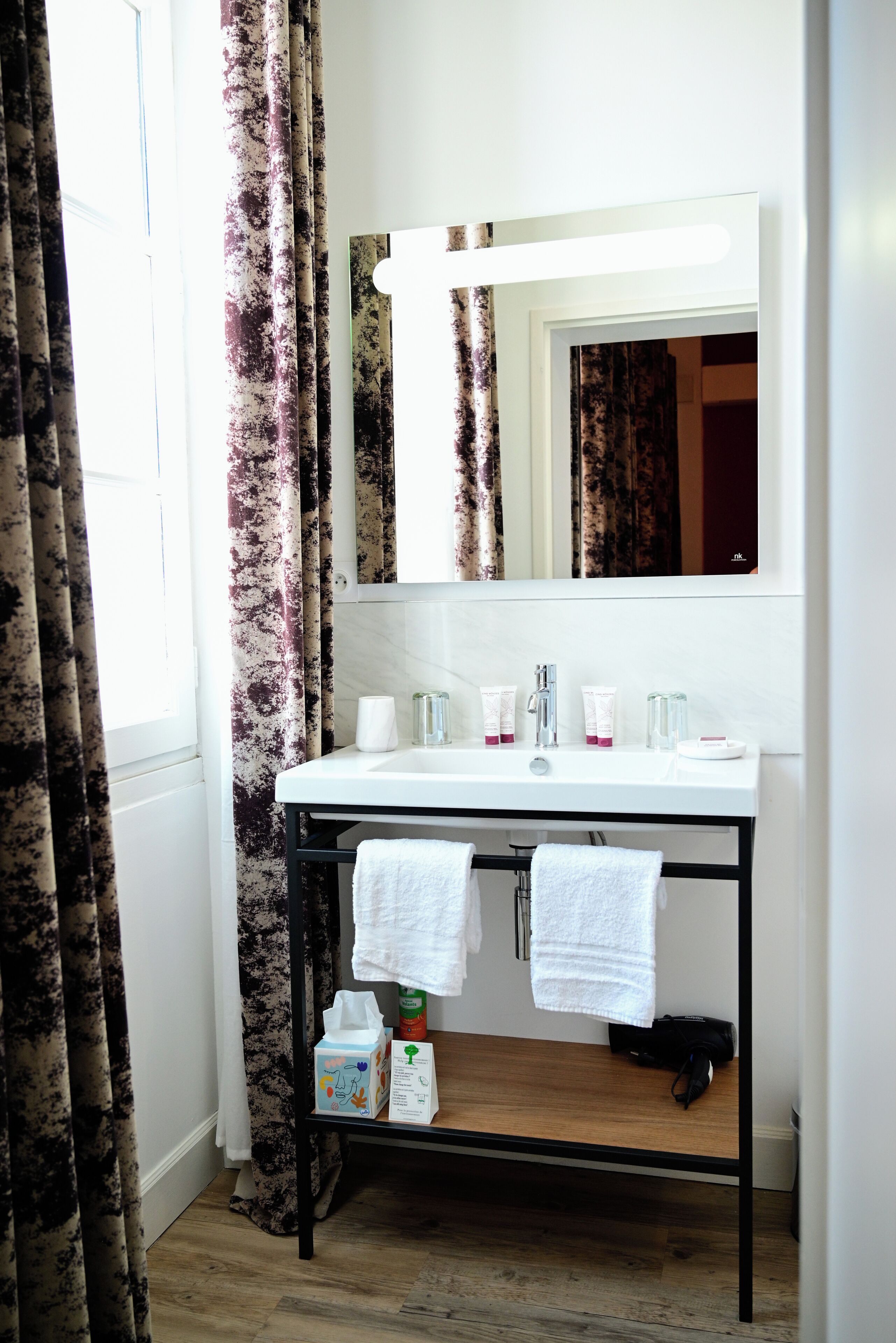 A bathroom with a white sink, a mirror, and a wooden shelf below the sink.