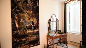 A room with a large zebra painting, a wooden desk with a chair, a mirror, and a window with curtains.