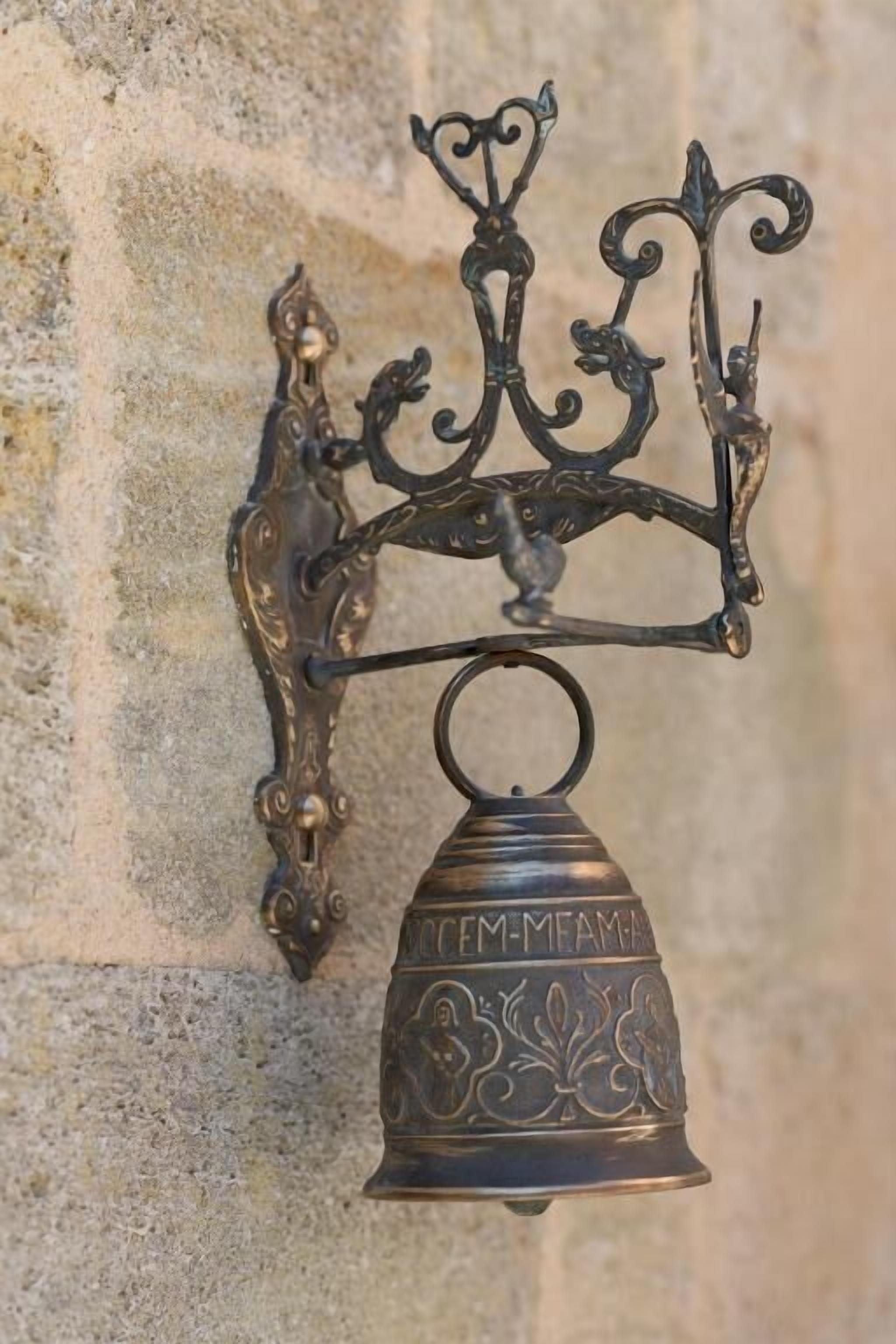 A wall-mounted metal bell with intricate designs and the inscription "TEM-MEM-MA".