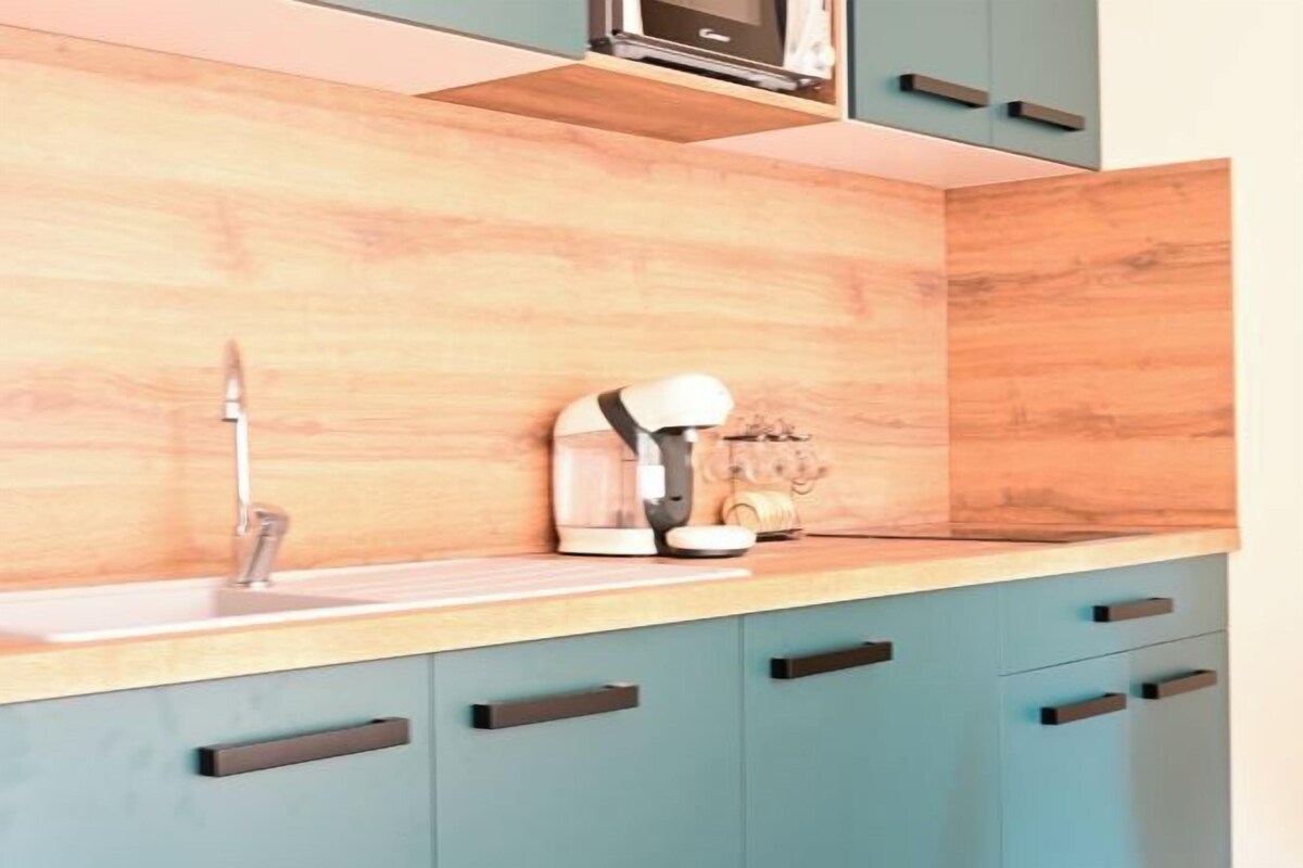 Una cocina con armarios color turquesa, encimera de madera y microondas sobre el fregadero.