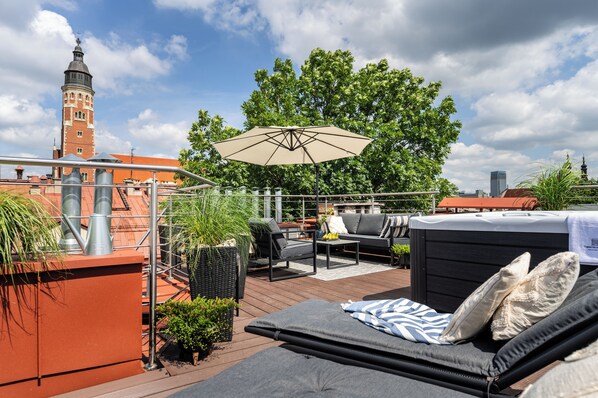 A rooftop terrace with outdoor furniture, a hot tub, and a view of a historic tower.