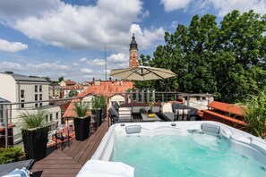 A rooftop terrace with a hot tub, outdoor seating, and a view of a historic tower.