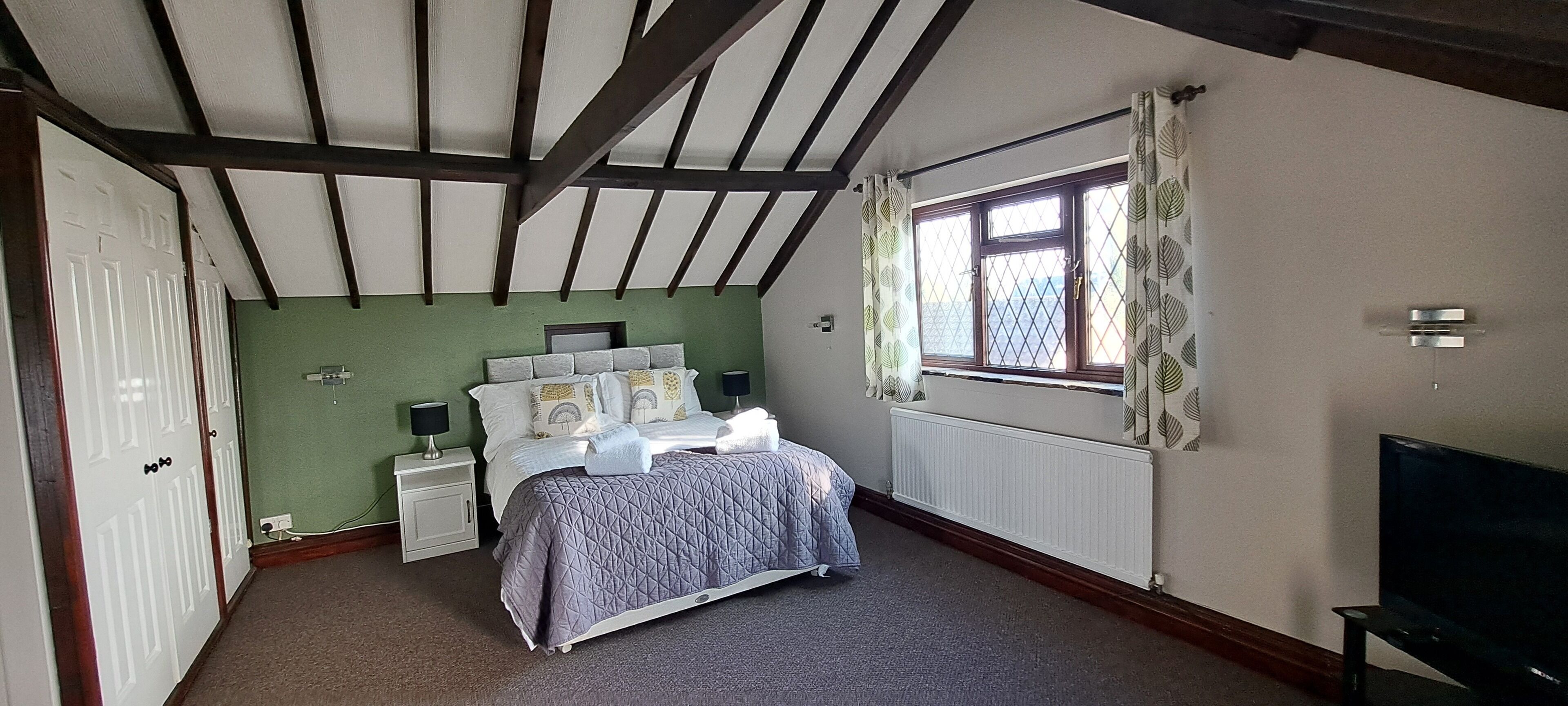 A bedroom with a bed, nightstands, a window with curtains, a radiator, and a TV.