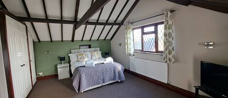 A bedroom with a bed, nightstands, a window with curtains, a radiator, and a TV.
