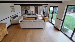 A spacious living room with a fireplace, large windows, and a wooden floor.