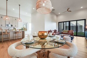 A modern kitchen with white cabinets, a dining area with a glass table, and a living room with a leather sofa.