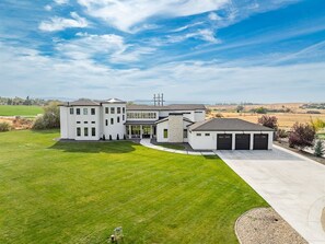 A modern two-story house with a large front lawn, garage, and a clear sky. - 14,000 SqFt Estate w/ Gym Theater Sauna Sleeps 40+ (Nampa)