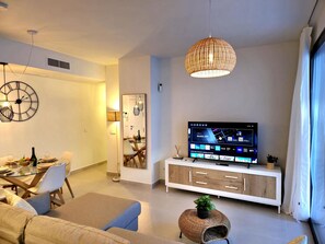 Un soggiorno moderno con zona pranzo, un televisore che mostra un'app mobile e un orologio grande appeso al muro.