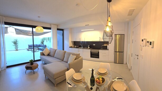 A modern living room with a sofa, dining table set for four, and a kitchen area with a refrigerator and microwave. - Luxury 2-Bedroom Apt with Jacuzzi, Patio & Parking 1km from Beach (Torremolinos)