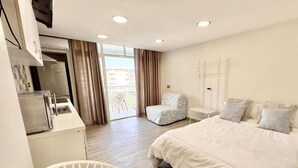 Ein Hotelzimmer mit Bett, Schreibtisch, Stuhl und einem Balkon mit Vorhängen.