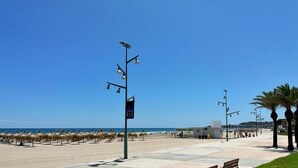Ein Strand mit Palmen, einem klaren Himmel und einem Gebäude in der Ferne.