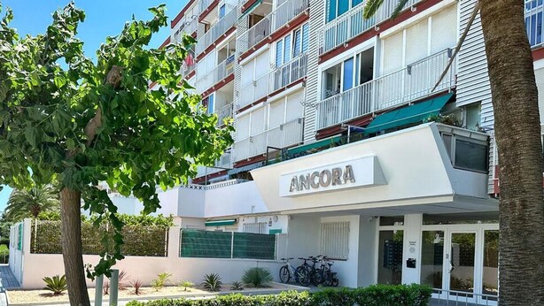 Ein modernes Hotel mit weißer Fassade, Balkonen und einem Schild mit der Aufschrift 'ANCORA'.
