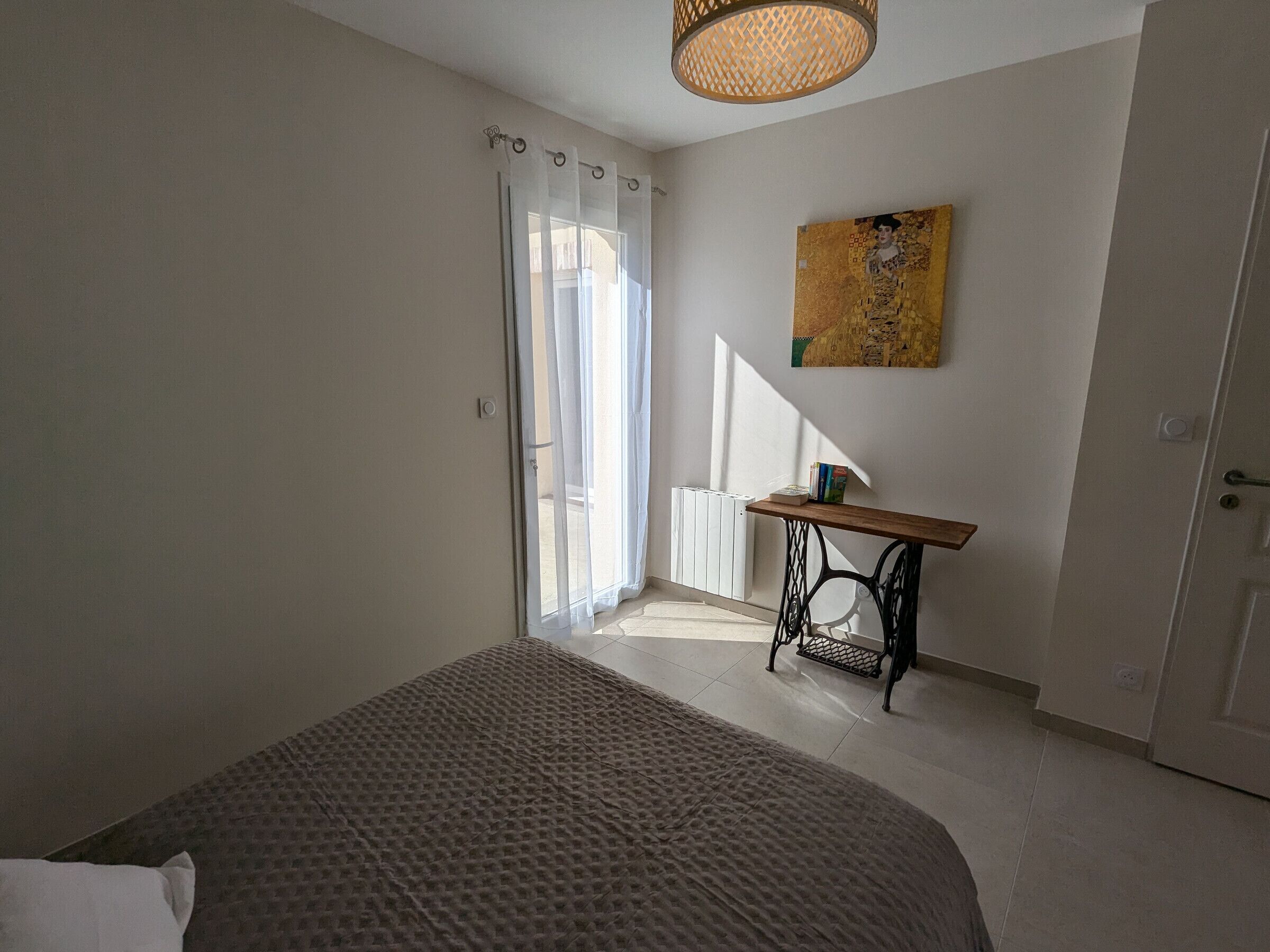 Quarto com cama, escrivaninha, radiador e um quadro na parede.