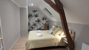 A bedroom with a sloped ceiling, a bed with a beige bedspread, two pillows, and a nightstand. - Charming renovated house in the heart of Loire Valley with parking and wifi (Chaingy)