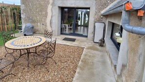 A patio with a tiled table and chairs, a covered grill, and a stone wall. - Charming renovated house in the heart of Loire Valley with parking and wifi (Chaingy)