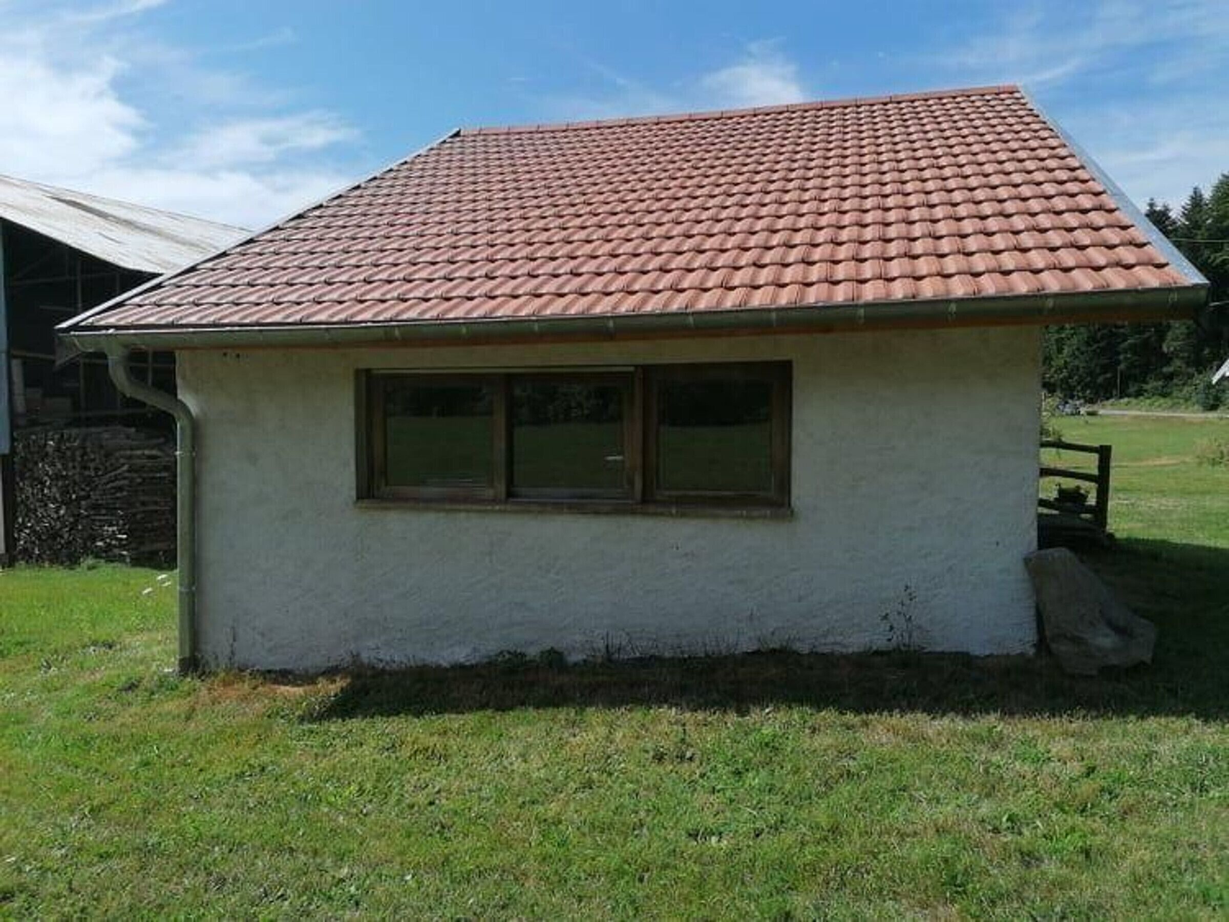 A small, single-story building with a red-tiled roof and a window.