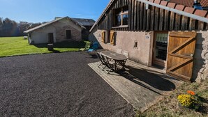Een landelijk gebouw met een stenen gevel en houten details, een grindpad en een klein terras met tuinmeubilair.