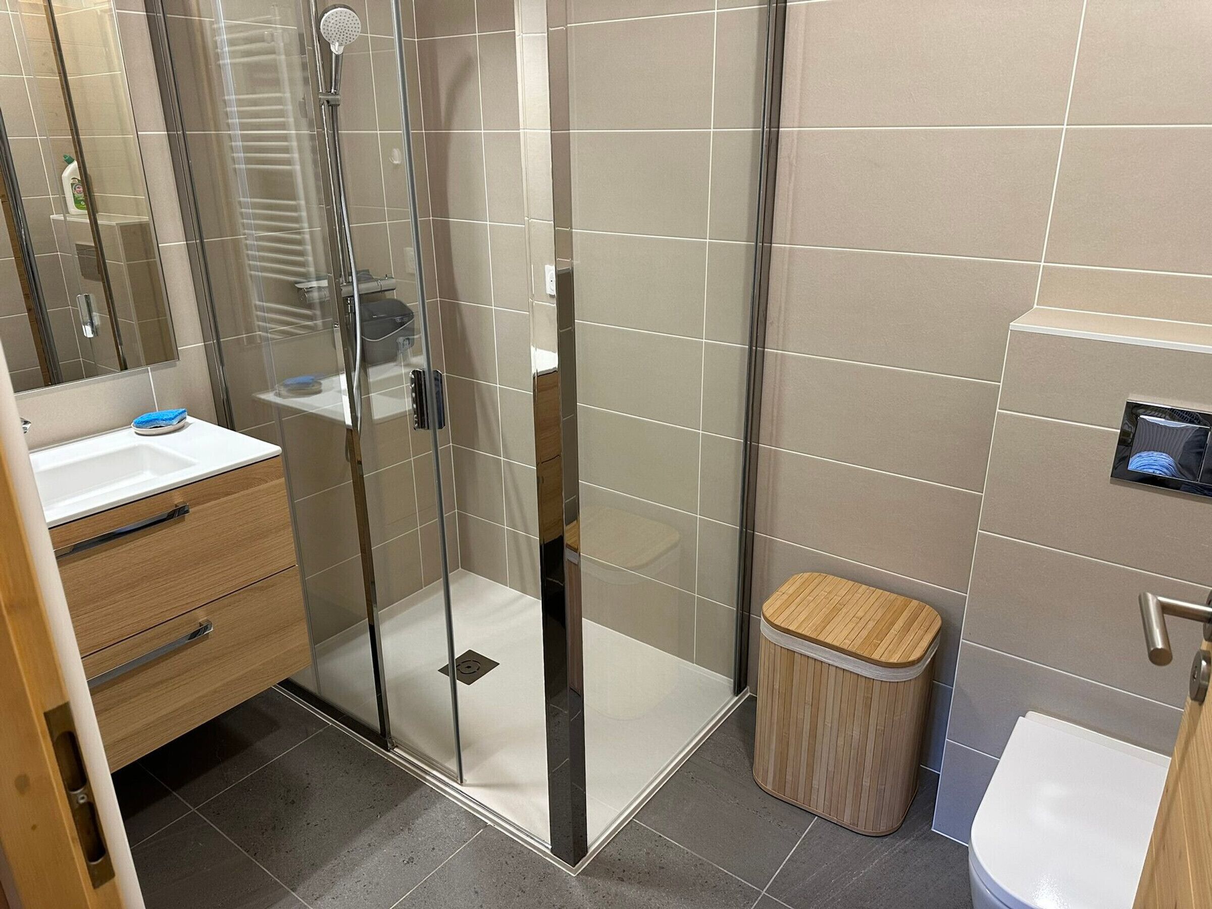 A modern bathroom with a glass-enclosed shower, a wooden vanity, and a toilet.
