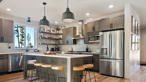 A modern kitchen with a central island, stainless steel appliances, and wooden bar stools. - The Basin is a modern, luxury cabin nestled in the pines at the base of Discovery Ski Hill. Enjoy panoramic views of the surrounding forest and the relaxing sounds of a nearby creek while relaxing by a smokeless fire in the Solo stove on the deck. (Philipsburg)