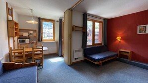 A compact room with a bed, a small table, a microwave, and a window with curtains.
