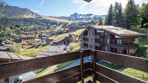 A mountain resort with chalet-style buildings, a ski lift, and a view of the surrounding mountains.