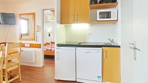 A compact kitchen with wooden cabinets, a microwave, a dishwasher, and a small dining area with a wooden chair. - Apartment 5 pers, parking, Plagne Soleil (Plagne Soleil)