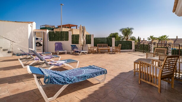 Une terrasse sur le toit, dotée de chaises longues, de mobilier en bois et offrant une vue sur les environs.