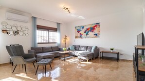 Un salon moderne avec un canapé d’angle, un fauteuil gris et une table basse. Un grand tableau représentant une carte du monde est accroché au mur, et une petite plante est posée sur une table d’appoint.