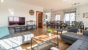 Un salon spacieux doté d’un grand téléviseur à écran plat, de canapés gris, d’une table basse et d’un coin repas avec des chaises et une table.
