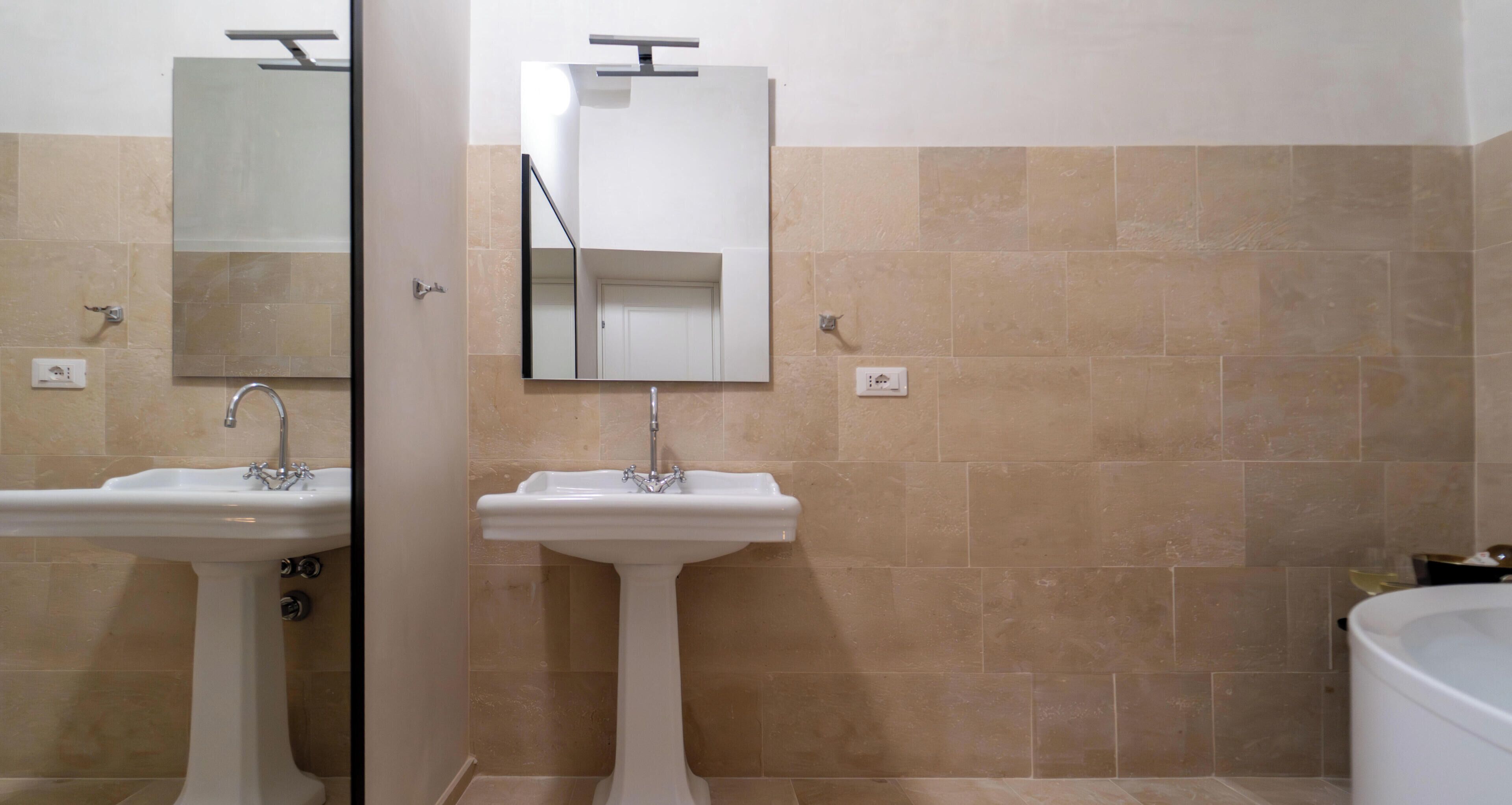 A bathroom with two sinks, a mirror, and beige tiled walls.