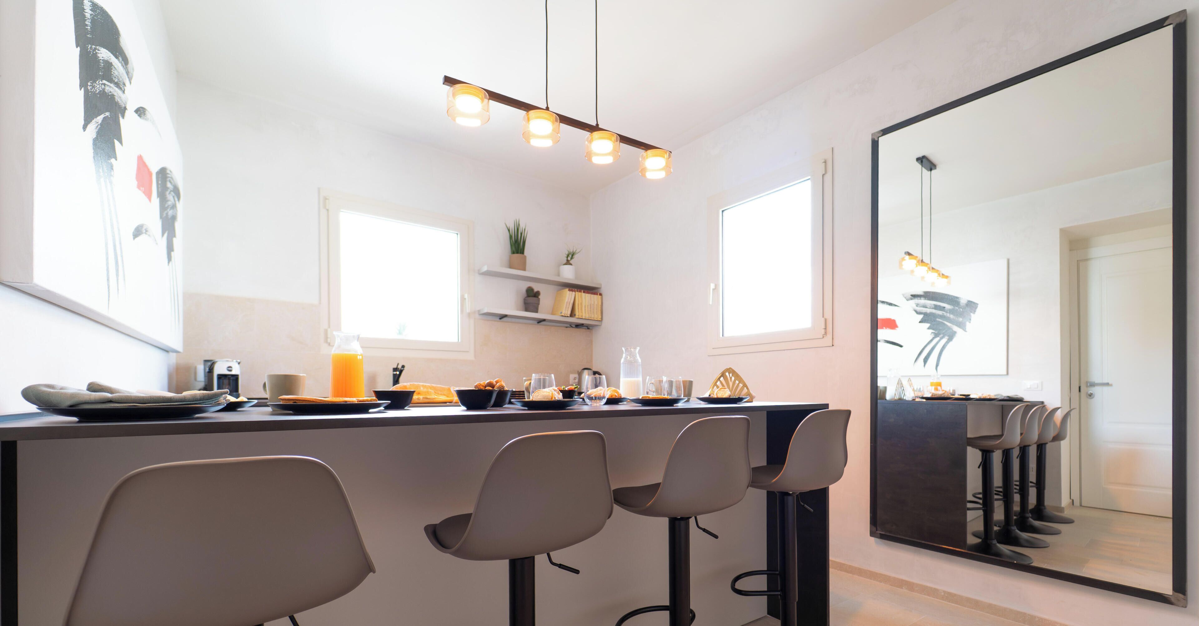 A modern kitchen with a bar area, pendant lighting, and a large mirror.