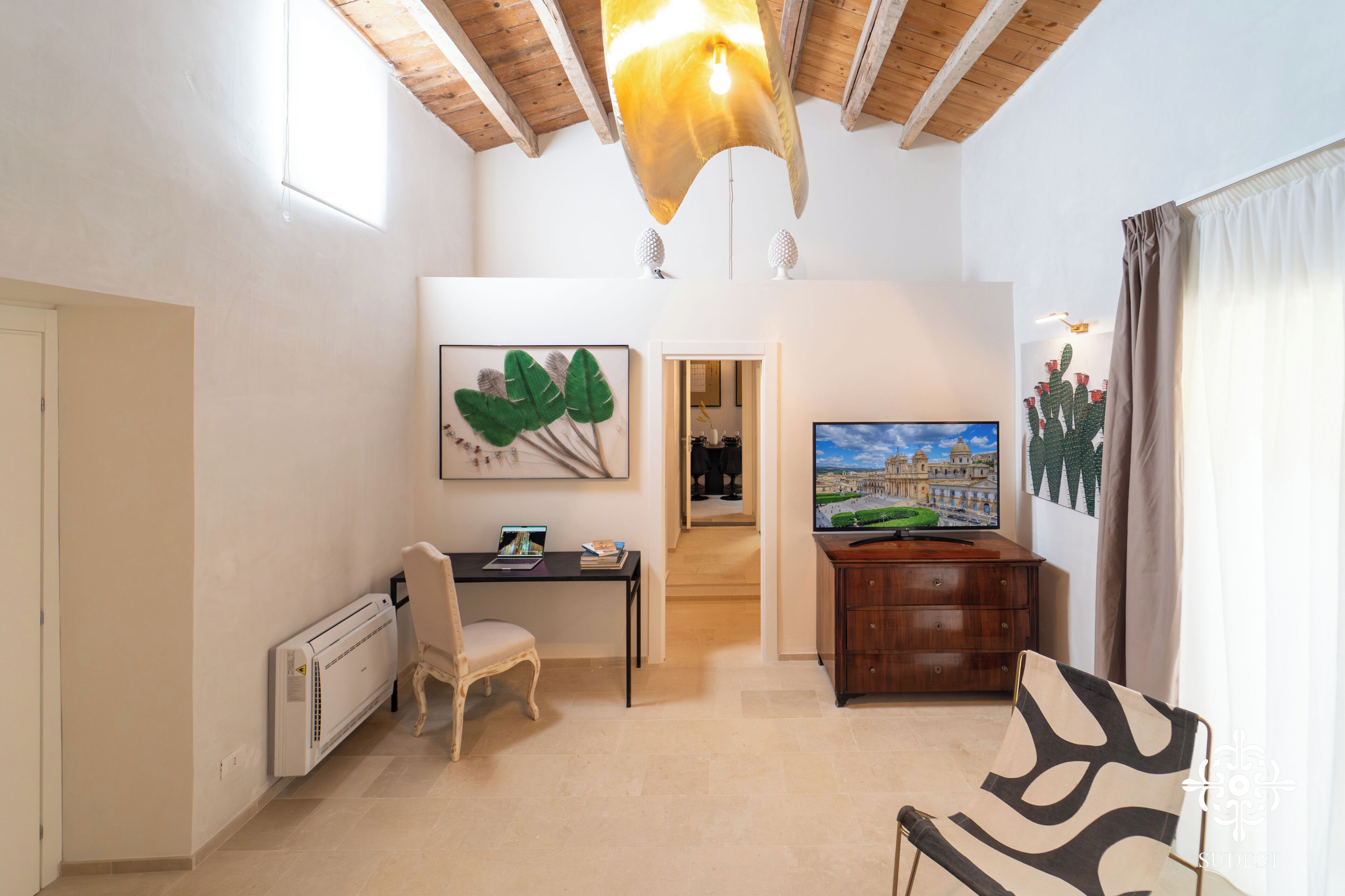A room with a desk, chair, radiator, television, and artwork.