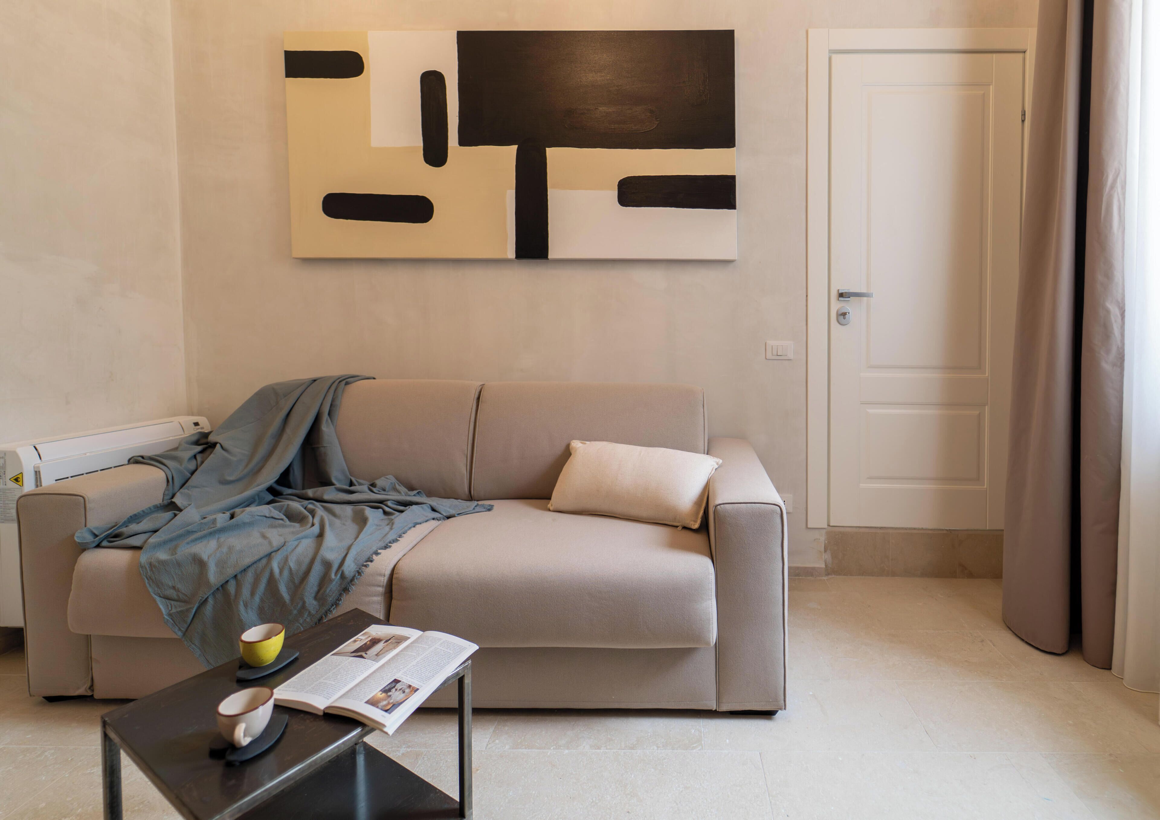 A living room with a sofa, a coffee table with a magazine, a wall with abstract art, and a door.