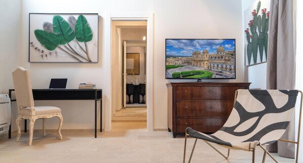 A room with a desk, chair, TV, and artwork.