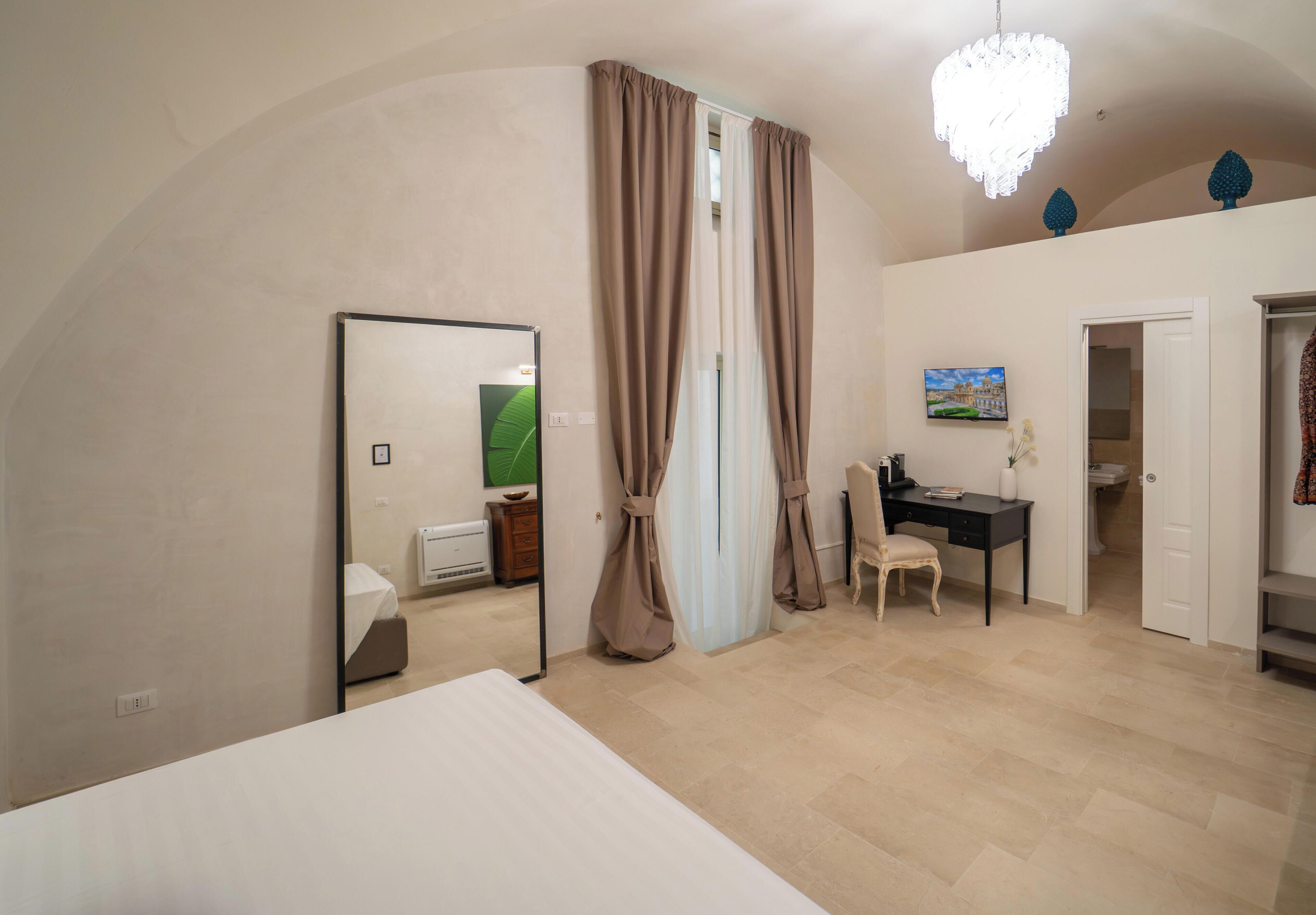 Ein Schlafzimmer mit einem Bett, einem Schreibtisch, einem Sessel, einem Spiegel und einer Deckenleuchte.